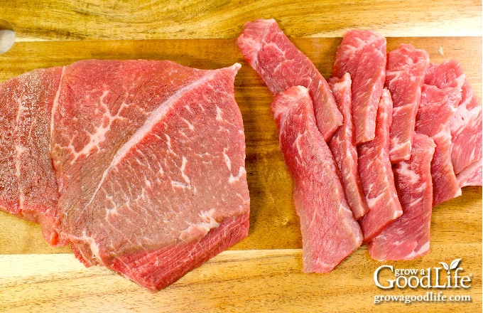 cutting steak into strips on a wooden cutting board