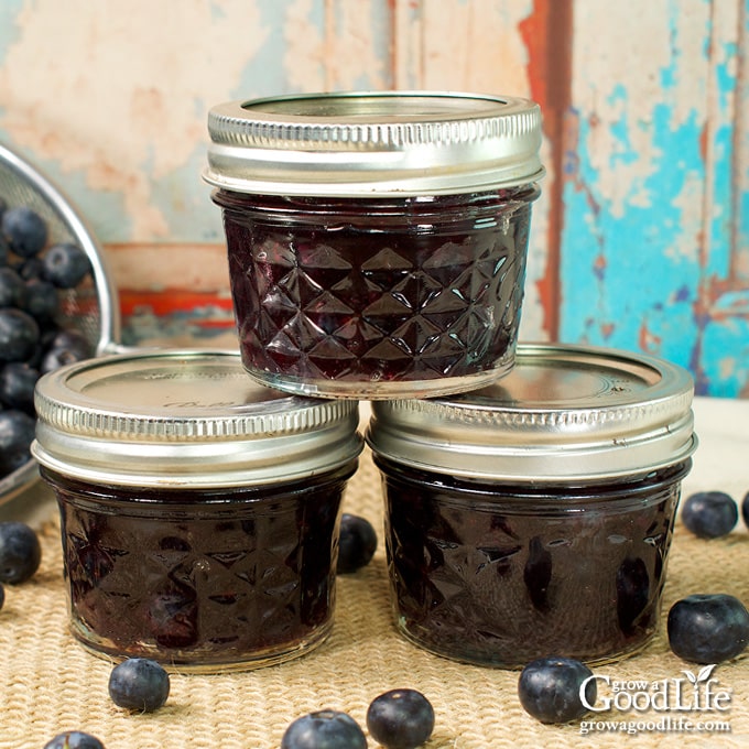 Jars of home canned blueberry syrup on a table.