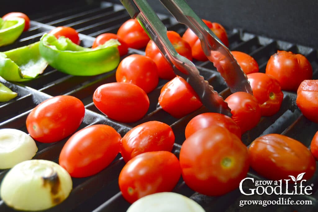 Action photo showing tongs flipping the tomatoes on the grill.