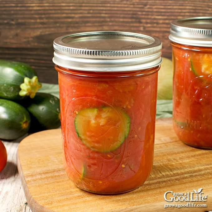 Jars of home canned zucchini with tomatoes on a table.