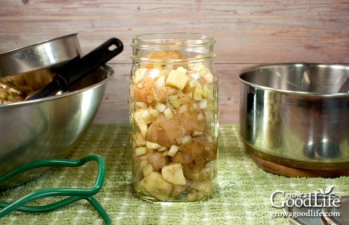 (Side view of raw packing a quart jar with chicken and gravy ingredients.