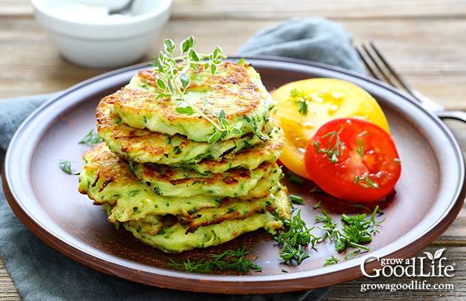 stack of zucchini pancakes and sliced tomatoes on a brown plate